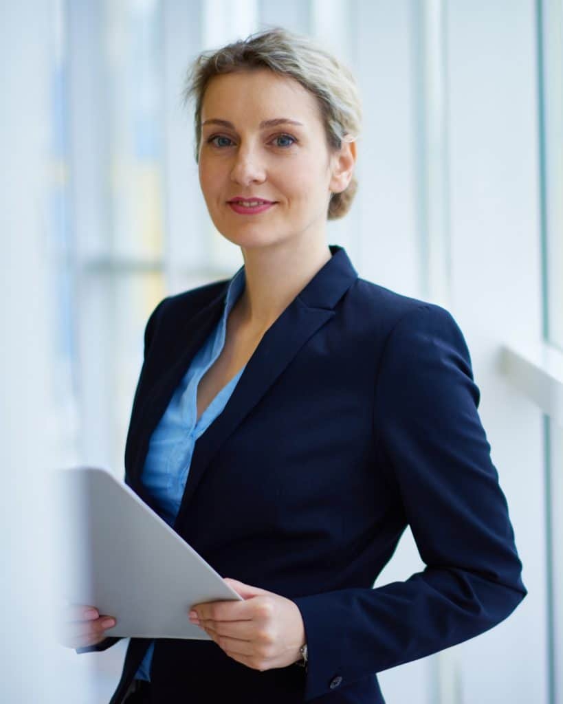 Mujer profesional con blazer azul y carpeta en oficina moderna.