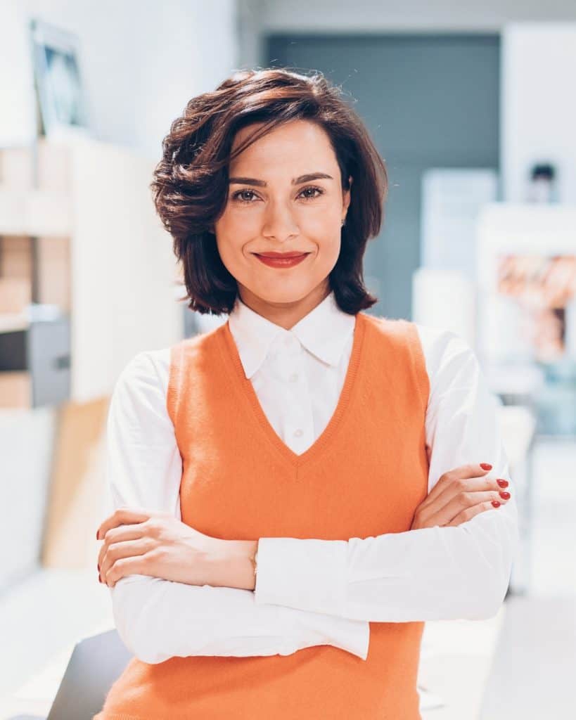 Mujer profesional sonriendo en oficina moderna con brazos cruzados.