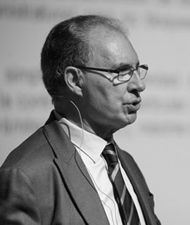 Hombre en traje y gafas hablando en una conferencia.